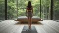 A woman standing barefoot on a Nexora grounding mat, with the connector and cord visible, in a room facing a forest.